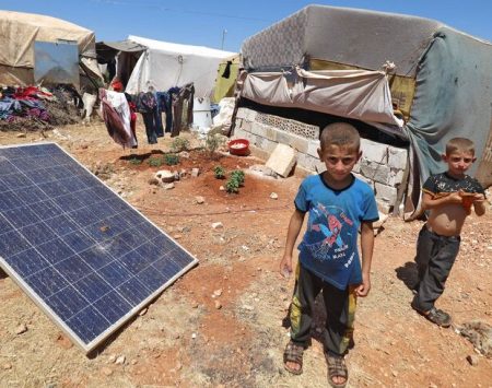 Children stand by a solar panel at a camp for Syrians displaced by conflict near the Syrian border with Turkey in the rebel-held northern part of the northwestern Idlib province amidst high temperatures on July 20, 2022. (Photo by Abdulaziz KETAZ / AFP) (Photo by ABDULAZIZ KETAZ/AFP via Getty Images)